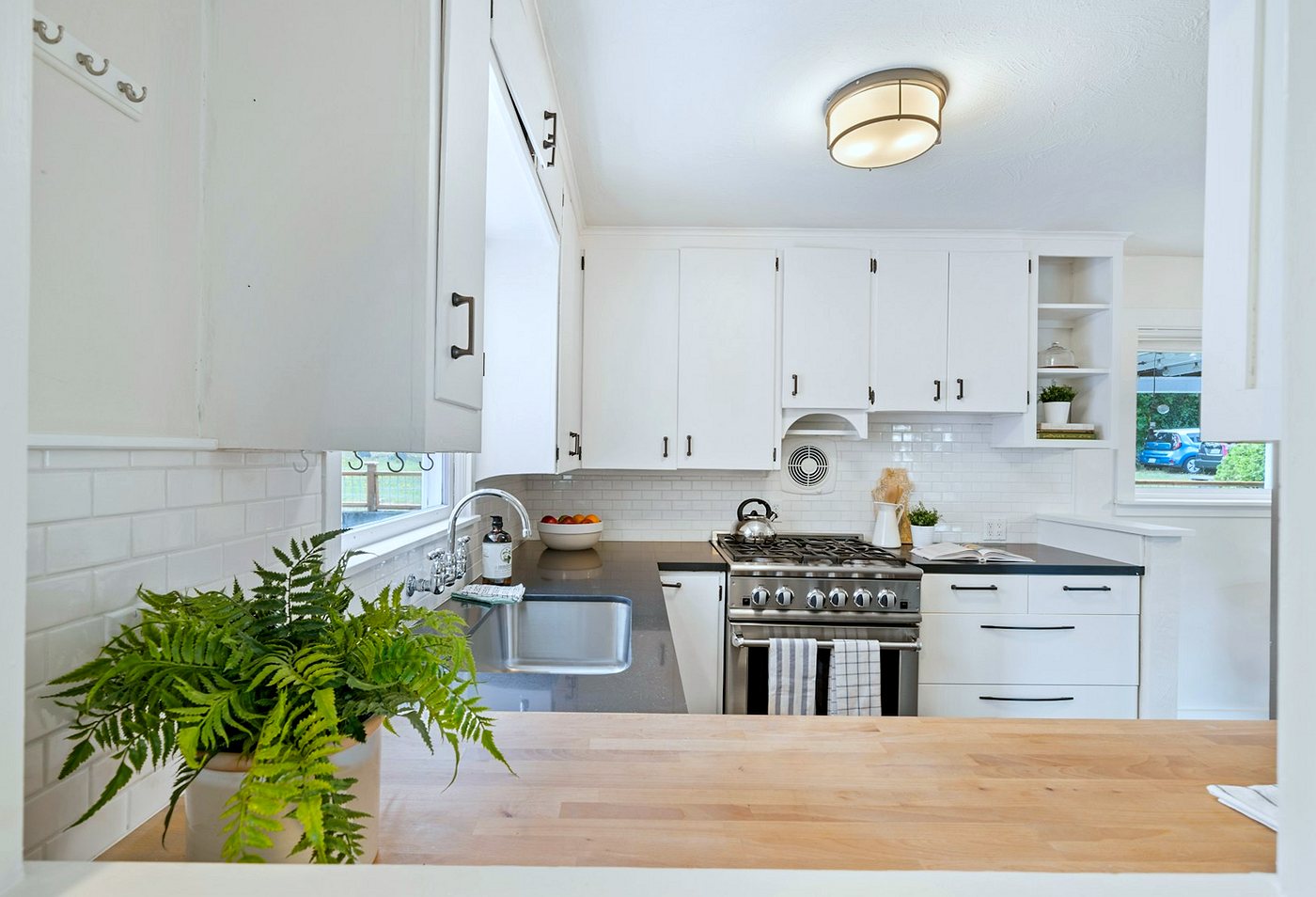 Compact white fitted kitchen with subway-tiled splashback, dark worktops and a timber breakfast bar